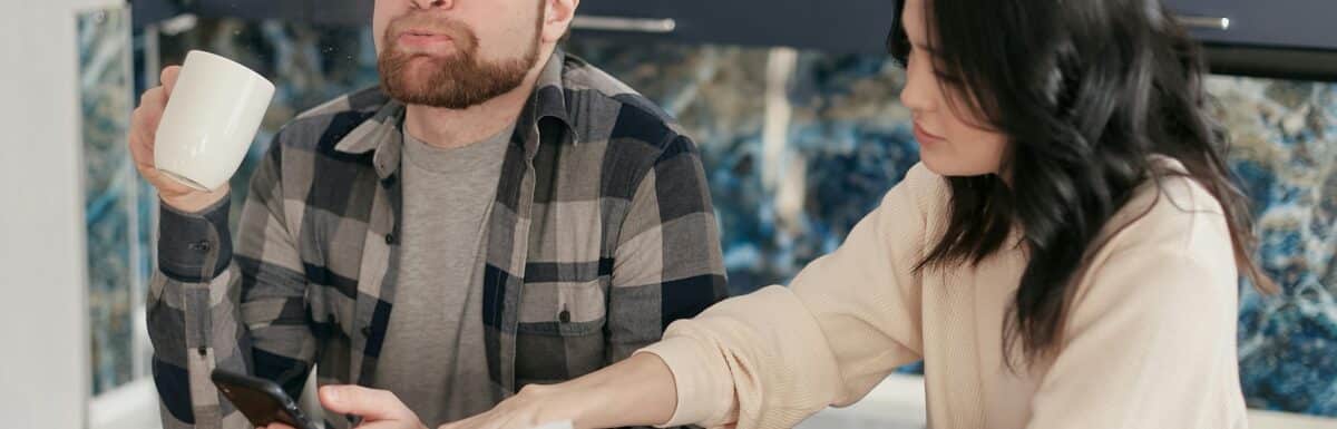 A couple looks worried as they review bills at their kitchen table, reflecting financial concerns.