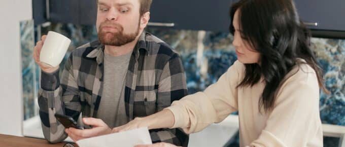 A couple looks worried as they review bills at their kitchen table, reflecting financial concerns.